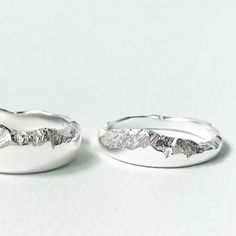 two silver rings with leaves on them sitting next to each other in front of a white background