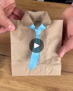 two hands holding a brown paper bag with a blue tie on it