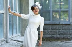 a woman in a white dress and hat leaning on a window sill with her arms outstretched