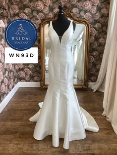 a white wedding dress on display in front of a floral wallpapered room with a mirror