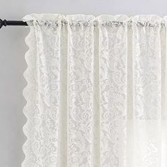 the curtain is hanging on a rod and has an intricate lace design in white color