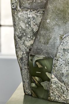 an abstract piece of art with moss and rocks on it's sides, sitting on a table in front of a window