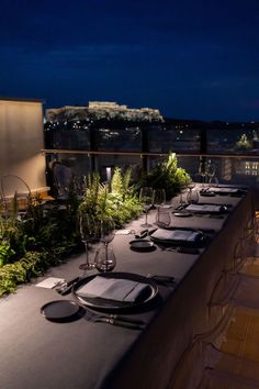 a long table with place settings on top of it at night, overlooking the city