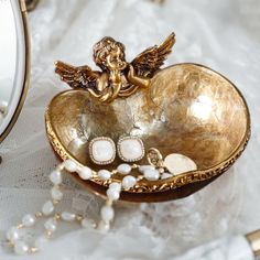 a gold heart shaped box with an angel decoration on it and pearls around the edges