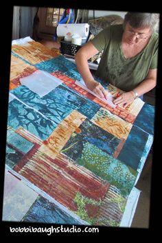 a woman sitting at a table working on a quilt