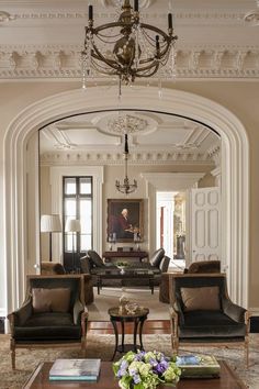 a living room filled with furniture and a chandelier hanging from the ceiling in front of a doorway