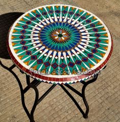 a small table with a colorful design on it's top sitting on the ground