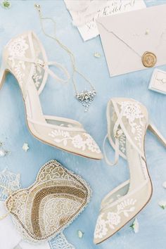 wedding shoes and jewelry laid out on a blue table with white flowers, pearls, and lace