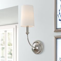 a wall light with a white shade on it in a living room next to two windows