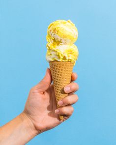 a hand holding an ice cream cone with yellow icing on it against a blue background