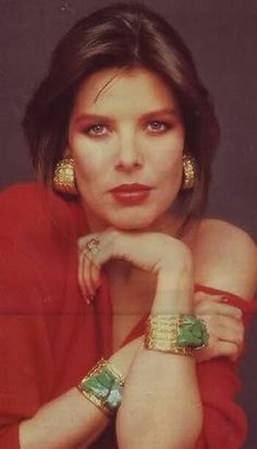 a woman in red shirt and gold bracelets posing with her arms on her chest