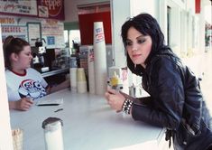 a woman sitting at a table with a cup in her hand and another person behind her