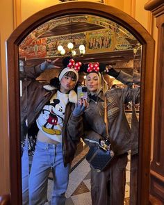 two people dressed up in mickey mouse ears taking a selfie with their cell phone