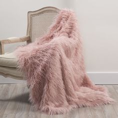 a fluffy pink blanket sitting on top of a wooden chair next to a white wall