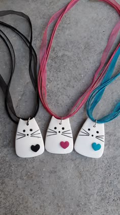 three necklaces with cats on them are sitting on the ground, one has a heart in its mouth