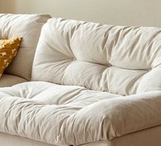 a white couch sitting in front of a window next to a wooden table with a yellow pillow on it