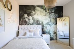 a white bed sitting next to a wall with flowers painted on it and a chandelier hanging from the ceiling