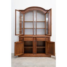 a large wooden cabinet with glass doors and cupboards on both sides, in front of a white wall