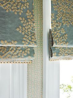 two windows with roman blinds in front of them and one window behind the blind that has gold leaves on it