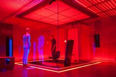 two mannequins are standing in an empty room with red light coming from the ceiling