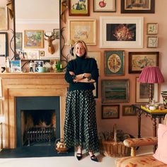 a woman standing in front of a fireplace with many pictures on the wall behind her