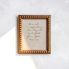 a gold frame with a handwritten quote on it against a white wall, next to a black cat