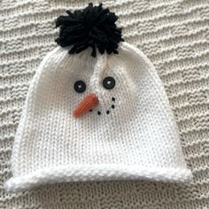 a knitted hat with a snowman's face on it sitting on top of a white blanket