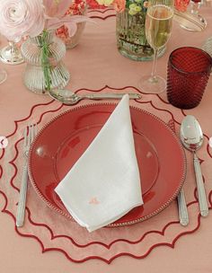 a red plate topped with a white napkin next to a glass vase filled with flowers