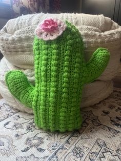 a crocheted cactus with a pink flower on its head sitting on a bed