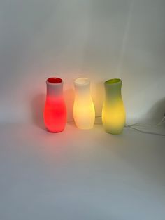 three different colored vases sitting next to each other on a white surface with wires