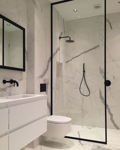 a bathroom with marble walls and flooring is pictured in this image, there is a shower stall next to the toilet