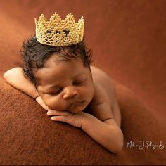 a baby wearing a golden crown laying on top of a brown blanket with his hands under his chin