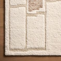 a white rug with squares and rectangles on top of wooden floor next to wall