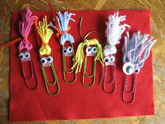 some paper clips with eyes and hair on them are sitting on a red cloth covered table