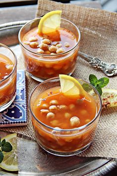 three glasses filled with soup and garnished with lemon wedges on a tray