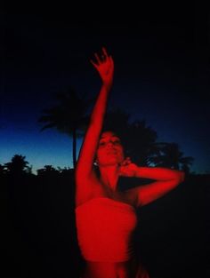 a woman in a red bathing suit reaching up to catch a frisbee at night