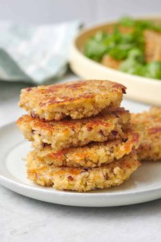 three crab cakes on a plate with a bowl of salad in the backround