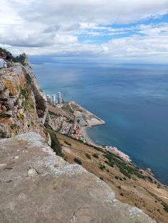 a man sitting on top of a cliff next to the ocean