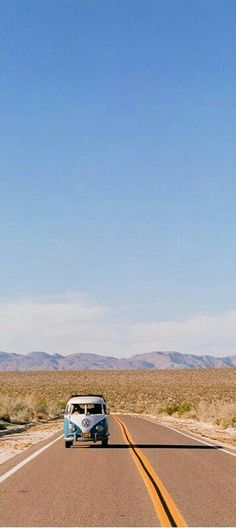 an old vw bus is driving down the road in the middle of the desert