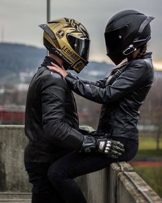 two people wearing helmets are sitting on a ledge