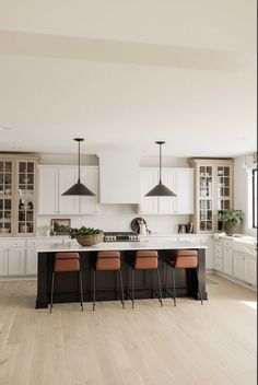 a large kitchen with white cabinets and wooden flooring is pictured in this image, there are four stools at the center of the island