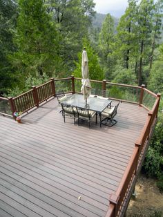 an outdoor table and chairs on a deck overlooking the woods with umbrellas over them