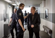 two men in suits talking to each other while others are walking down the hallway behind them