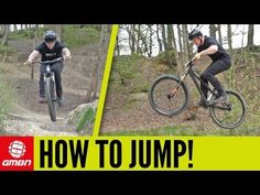 two men riding mountain bikes in the woods, one jumping over a jump and another on a bike