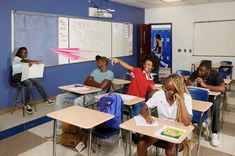 a group of people sitting at desks in a classroom with one person pointing to the side