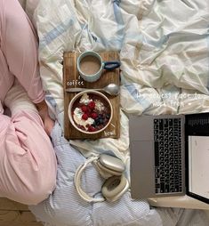 a person laying in bed with their laptop and breakfast on the table next to them