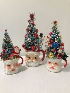 three santa claus mugs with christmas trees on them and ornaments in the shape of santa's heads