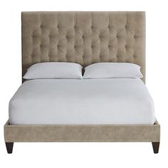 an upholstered bed with white sheets and pillows