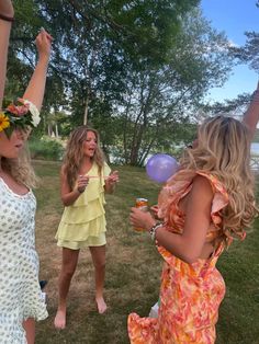 three women are standing in the grass and one is holding some balloons with her hand