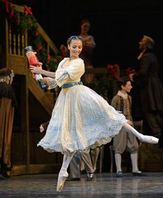 a young ballerina is dancing on stage with other dancers in the background and dressed in period costumes